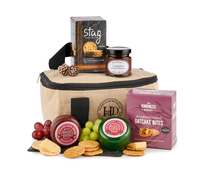 A cheese cool bag with a variety of gourmet cheeses and accompaniments such as biscuits, chutney, and oatcake bites, presented alongside fresh grapes and crackers.