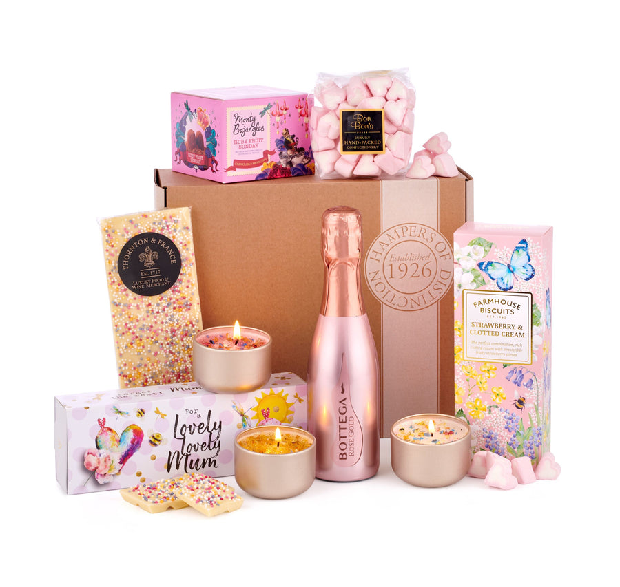 A Prosecco gift box laid out on a white table top. It contains rose prosecco from Bottega, scented candles for a lovely, lovely mum, farmhouse biscuits, strawberry bon bons, white chocolate and more. 