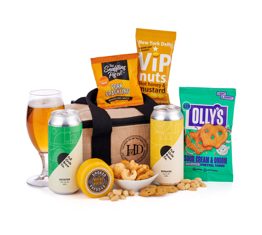 The Beer Cool Bag, featuring pale ales from Full Circle Brew Co. alongside savoury snacks to compliment the beers from this award winning brewery. Pork Crackling from the Snaffling Pig Co., Olly's Sour Cream & Onion & Smoked Cheddar from The Mouse House are just a few of the treats laid out around the beer & reusable cool bag. An unusual Beer Gift idea laid out on a white table top.